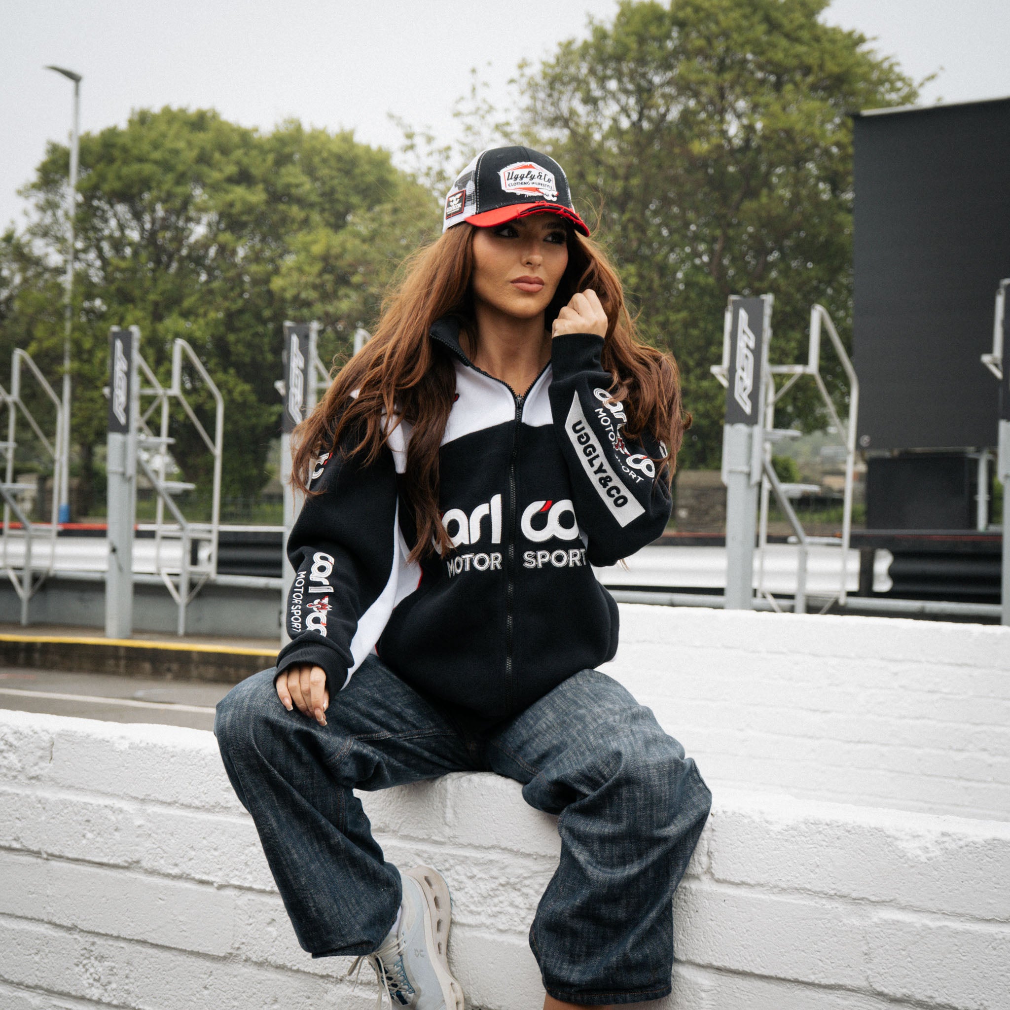 Female model styling the Carl Cox Motorsport track jacket beside the race paddock.
