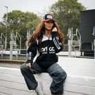 Female model styling the Carl Cox Motorsport track jacket beside the race paddock.