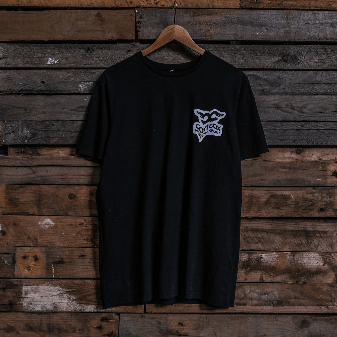 Front view of a Carl Cox Motorsport black t-shirt with car graphic and 'carl cox motorsport' logo on a wooden background