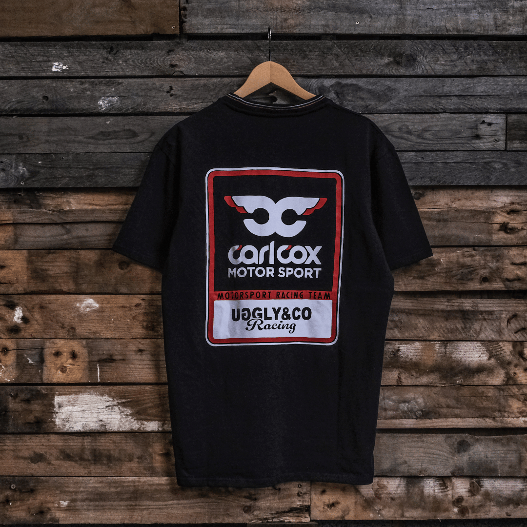Rear view of a Carl Cox motorsport black t-shirt with an Uggly&Co logo on a wooden background