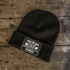 A black beanie with a logo on the cuff, placed on a wooden surface.
