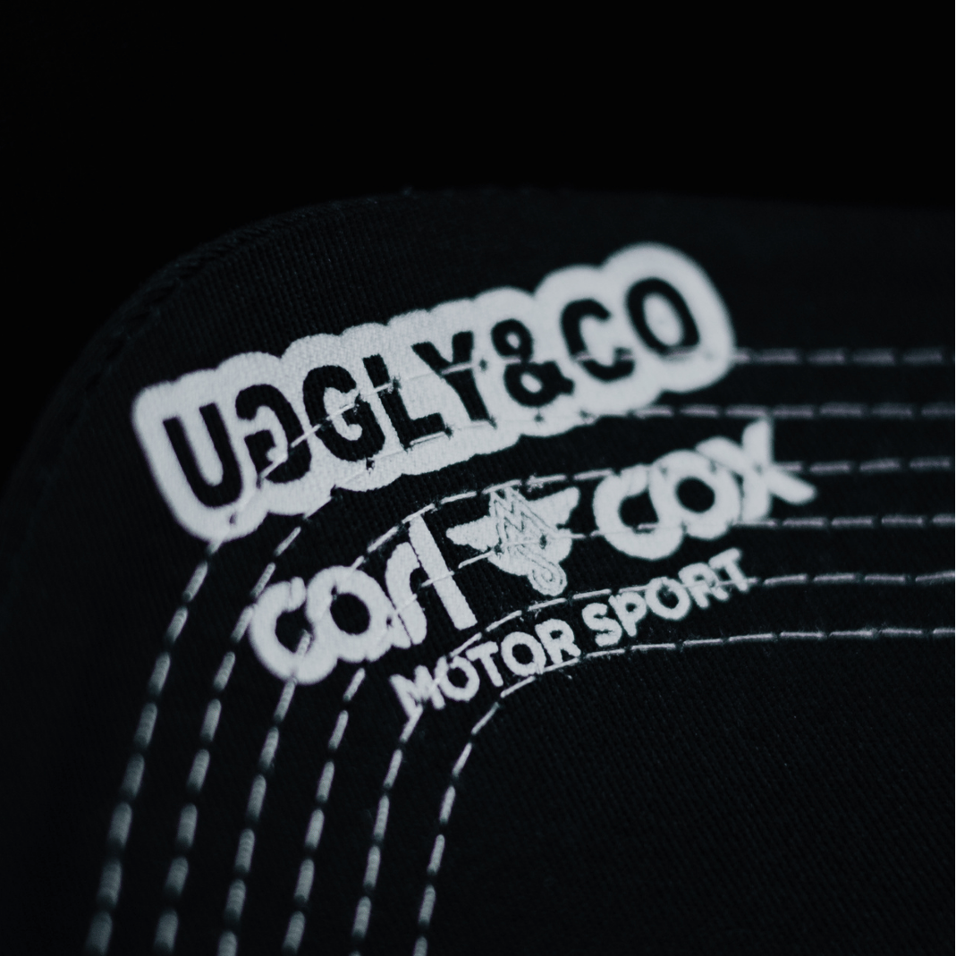 Close up of the Uggly&Co and Carl Cox Motorsport logos on the under side of the peak of an Official Carl Cox Motorsport Merchandise trucker hat in black and white