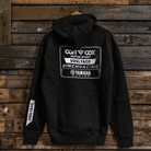 A black hoodie with white and grey text and logos, including 'Carl Cox Motorsport' and 'Uggly&Co', displayed on a wooden background.