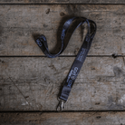 A black and silver lanyard with text and logos related to Carl Cox Motorsport and The Black Dub, laid out on a wooden surface.