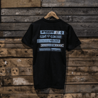 A black crew neck t-shirt with a graphic design in the center, featuring text and a cassette tape motif. The t-shirt is displayed on a wooden background.
