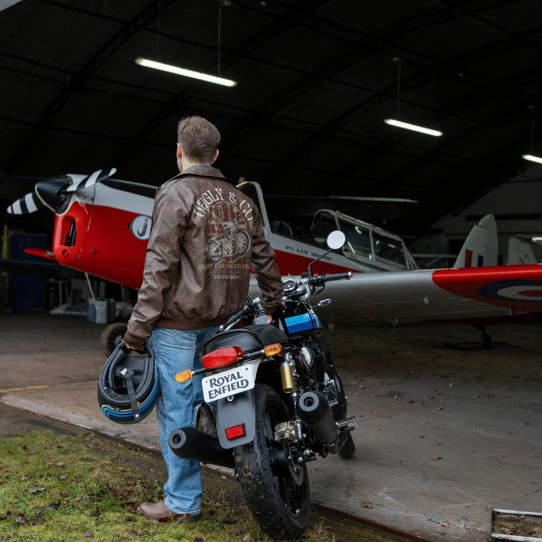 Man standing next to a motorcycle with a red and white airplane in the background