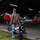 Man standing next to a motorcycle with a red and white airplane in the background