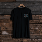 Front view of a Carl Cox motorsport black t-shirt with a colourful graphic design on a wooden wall