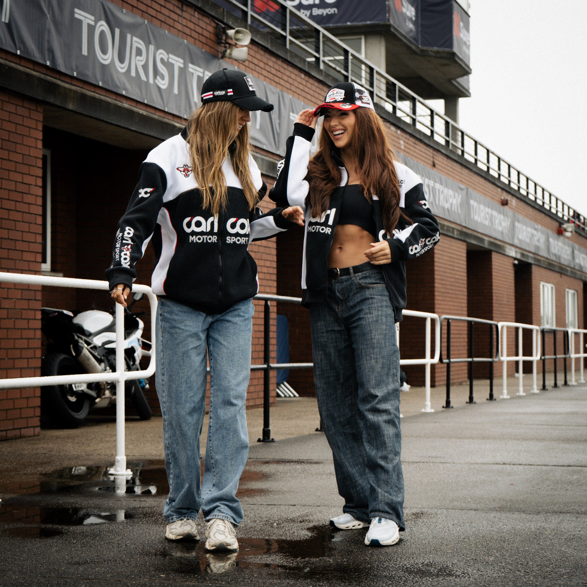 Female models wearing a Carl Cox Motorsport track jacket at a motorsport event.