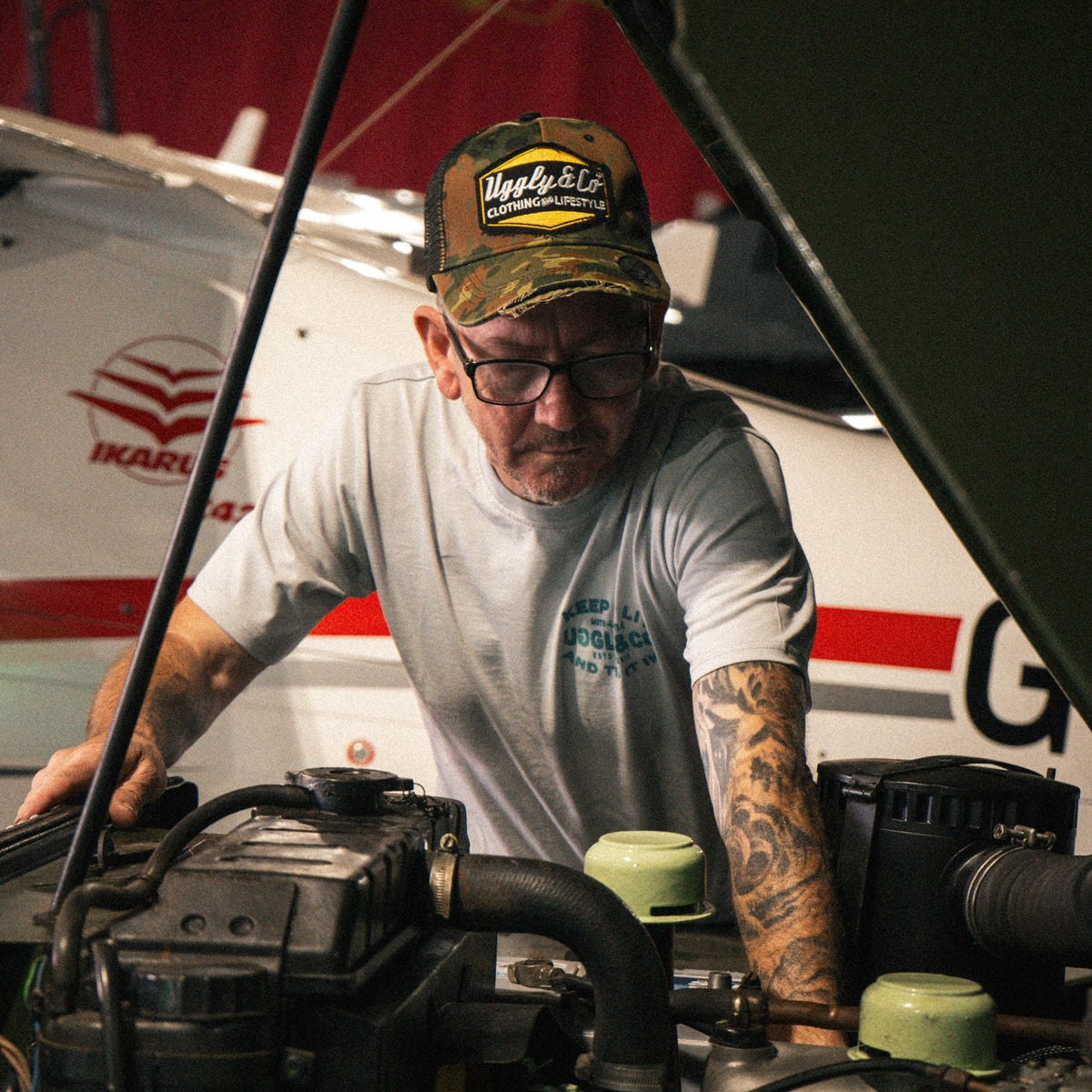 Man wearing a Green Camo Diamond Trucker Hat while working on a Land Rover in a workshop.