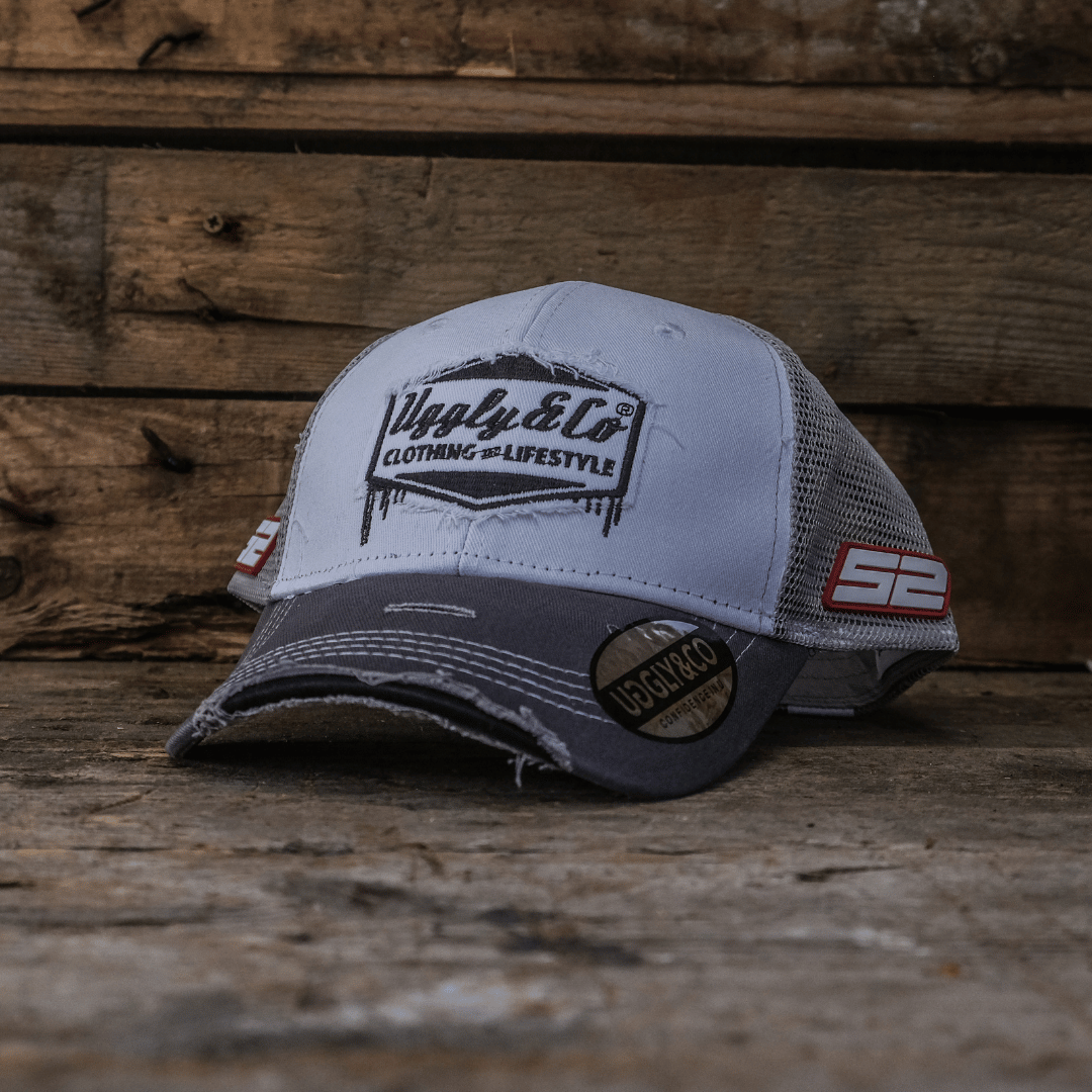 Grey and white trucker hat with Uggly&Co branding on a wooden background