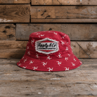 Red bucket hat with white Isle of Man Flag  patterns and a Uggly&Co logo on a wooden background