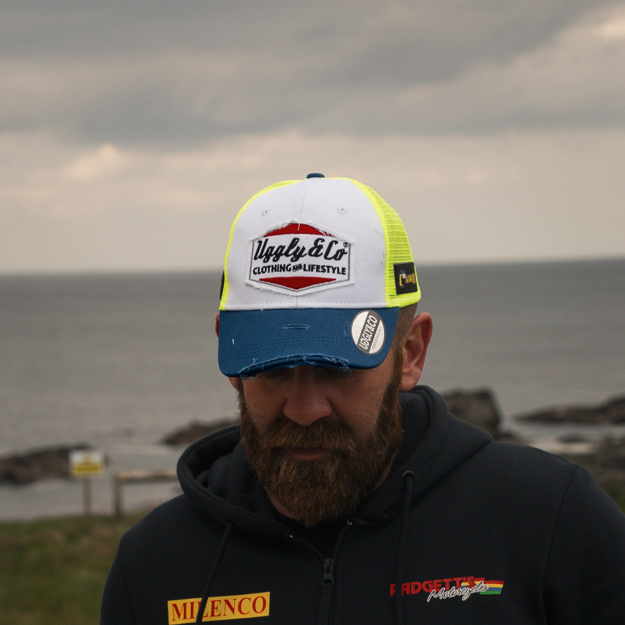 Jamie Coward showing trucker hat with head down near the beach