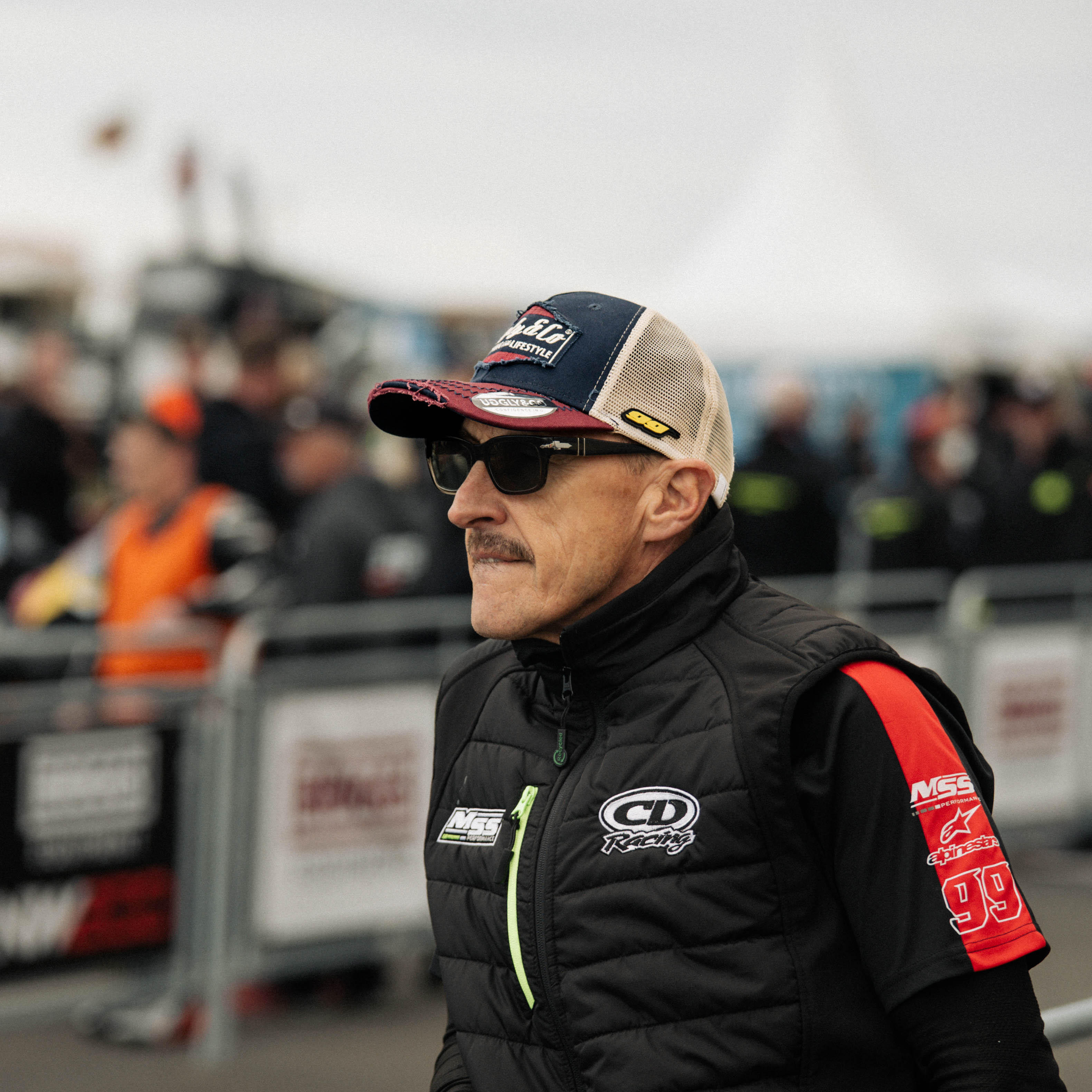 Jeremy McWilliams in the pit lane, stood wearing a hat and sunglasses on racetrack grid