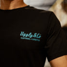 Close up view of a the chest logo of a Josh Brookes signature diamond black t-shirt with a blue Uggly&Co logo and a blurred background