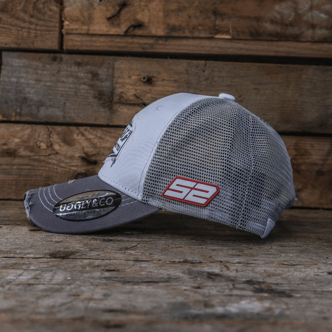 Grey and black trucker hat side view with mesh back and 52 on the side on a wooden surface