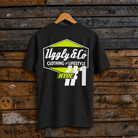 Rear view of an Uggly & Co and Kyle Ryde #1 diamond graphic black t-shirt  with white and lime green accents on a wooden background