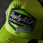 Close-up of the diamond logo on the Uggly & Co Fluro Diamond Trucker Hat x Kyle Ryde, photographed against a concrete floor.