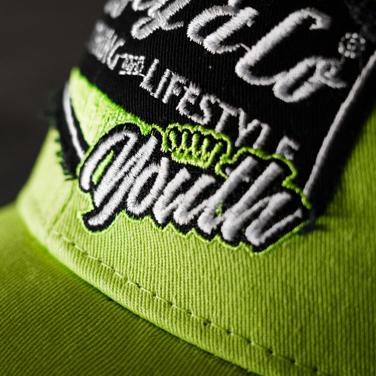 Close-up of the youth logo on the Uggly & Co Fluro Diamond Trucker Hat x Kyle Ryde, photographed against a concrete floor.