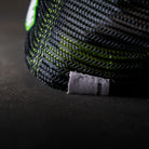 Close-up of the mesh panelling on the Uggly & Co Fluro Diamond Trucker Hat x Kyle Ryde, photographed on a concrete floor, highlighting the breathable trucker cap design.