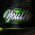 Close-up of the Youth badge on the Uggly & Co Fluro Diamond Trucker Hat x Kyle Ryde, photographed on a concrete floor, highlighting the badge detail on the British Superbikes inspired cap.