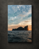 Rocky island rising from the ocean beneath a softly lit sunset sky, shown as coastal canvas wall art.