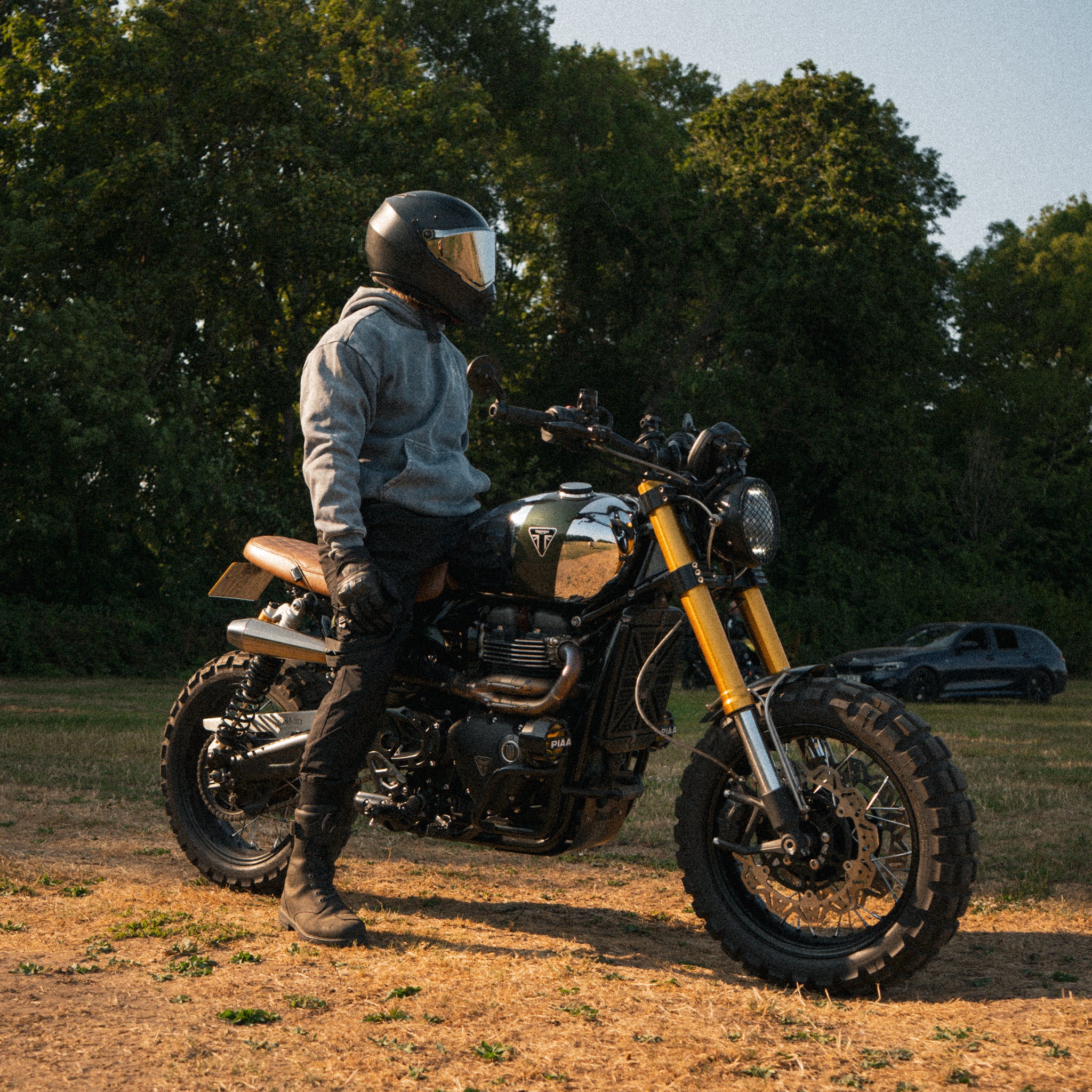 Man wearing an acid wash hoodie on a Triumph Scrambler motorcycle during a golden hour sunset.