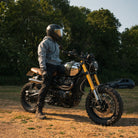 Man wearing an acid wash hoodie on a Triumph Scrambler motorcycle during a golden hour sunset.