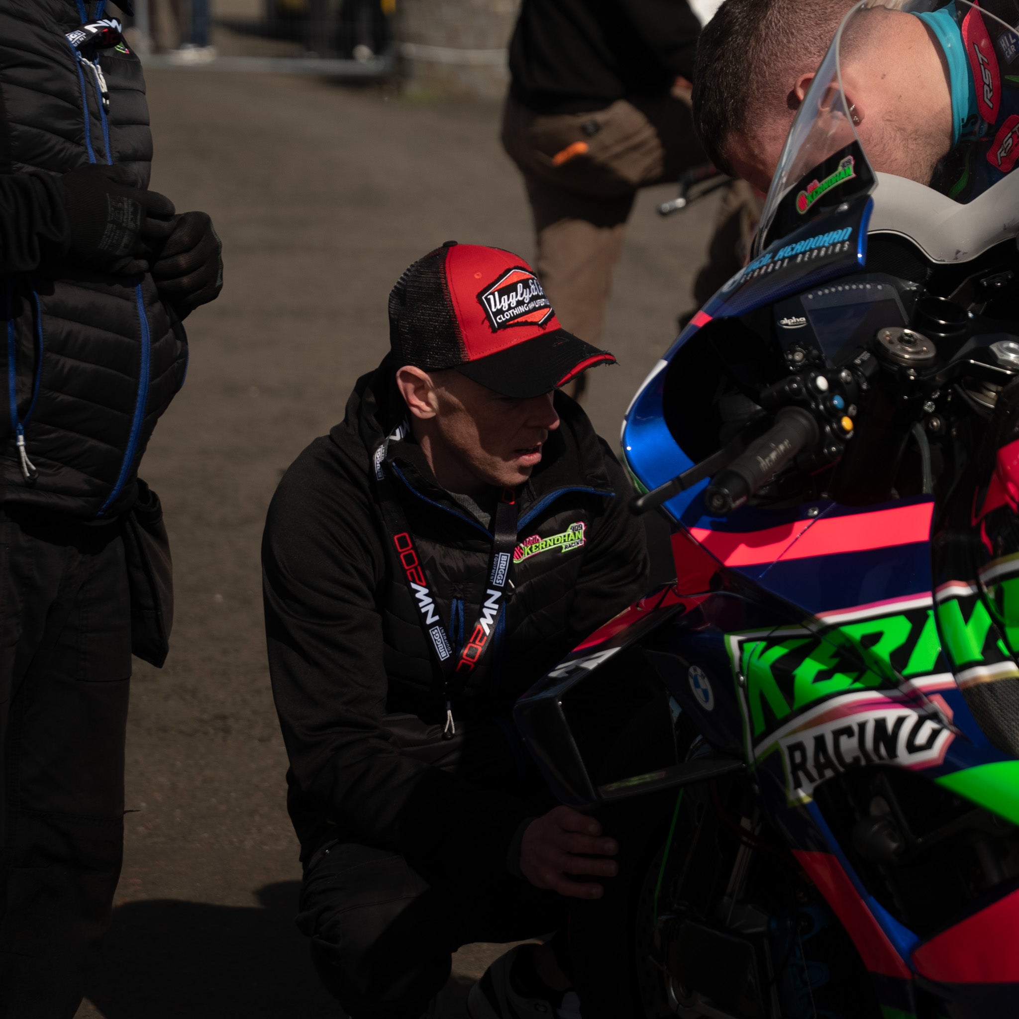 Man wearing black and red trucker hat working on a motorbike in a pit lane