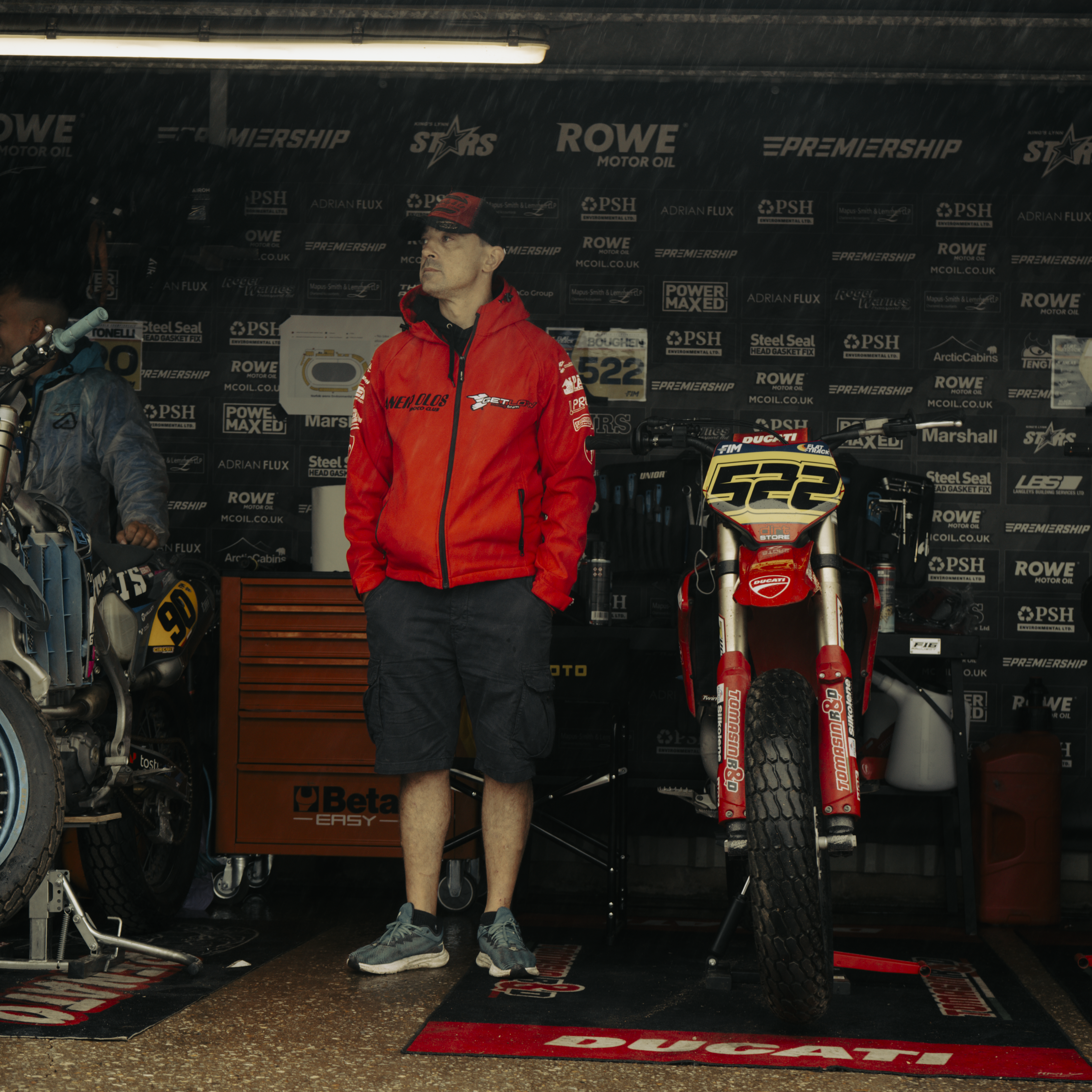Mechanic wearing the Black & Red Flat Track Trucker Hat while working in the paddock, showing the cap’s rugged motorsport style.