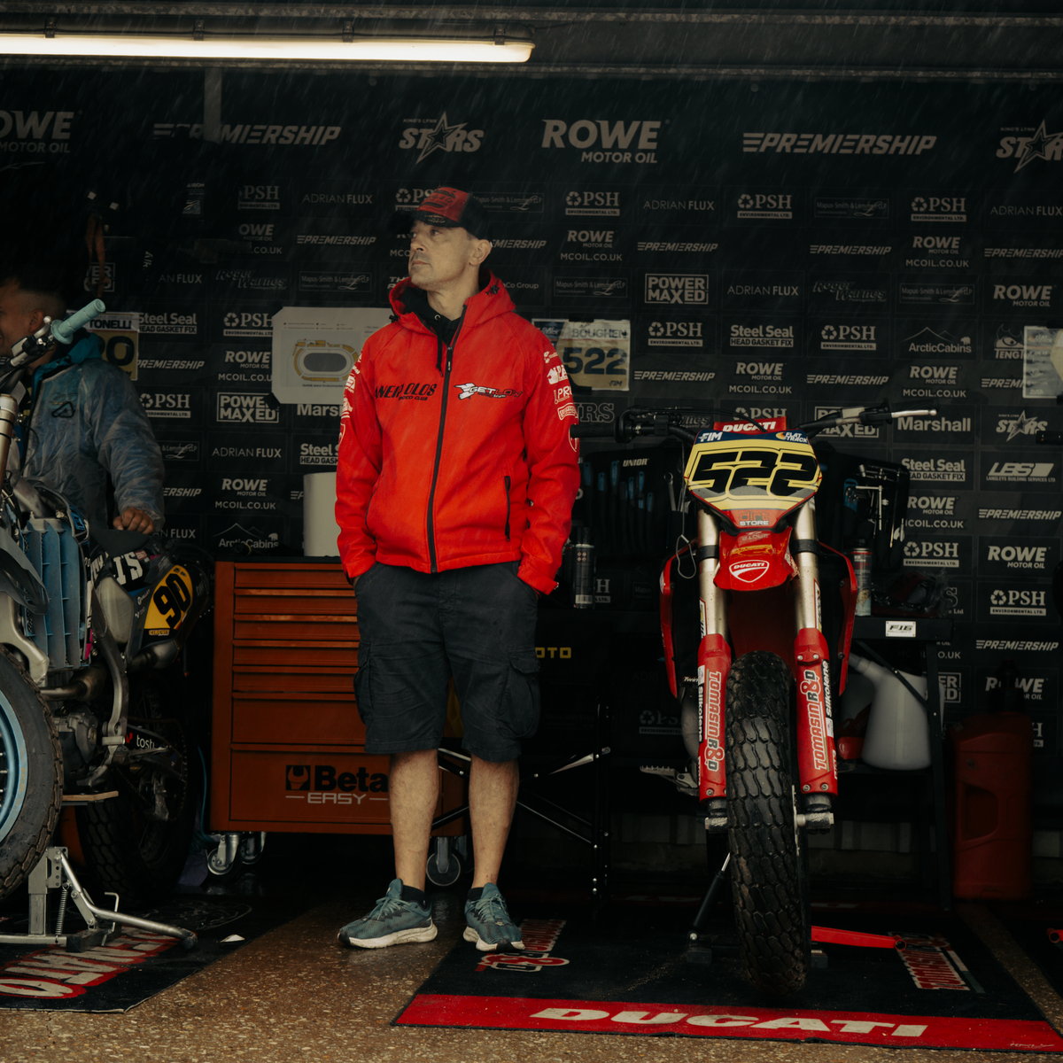 Mechanic wearing the Black & Red Flat Track Trucker Hat while working in the paddock, showing the cap’s rugged motorsport style.