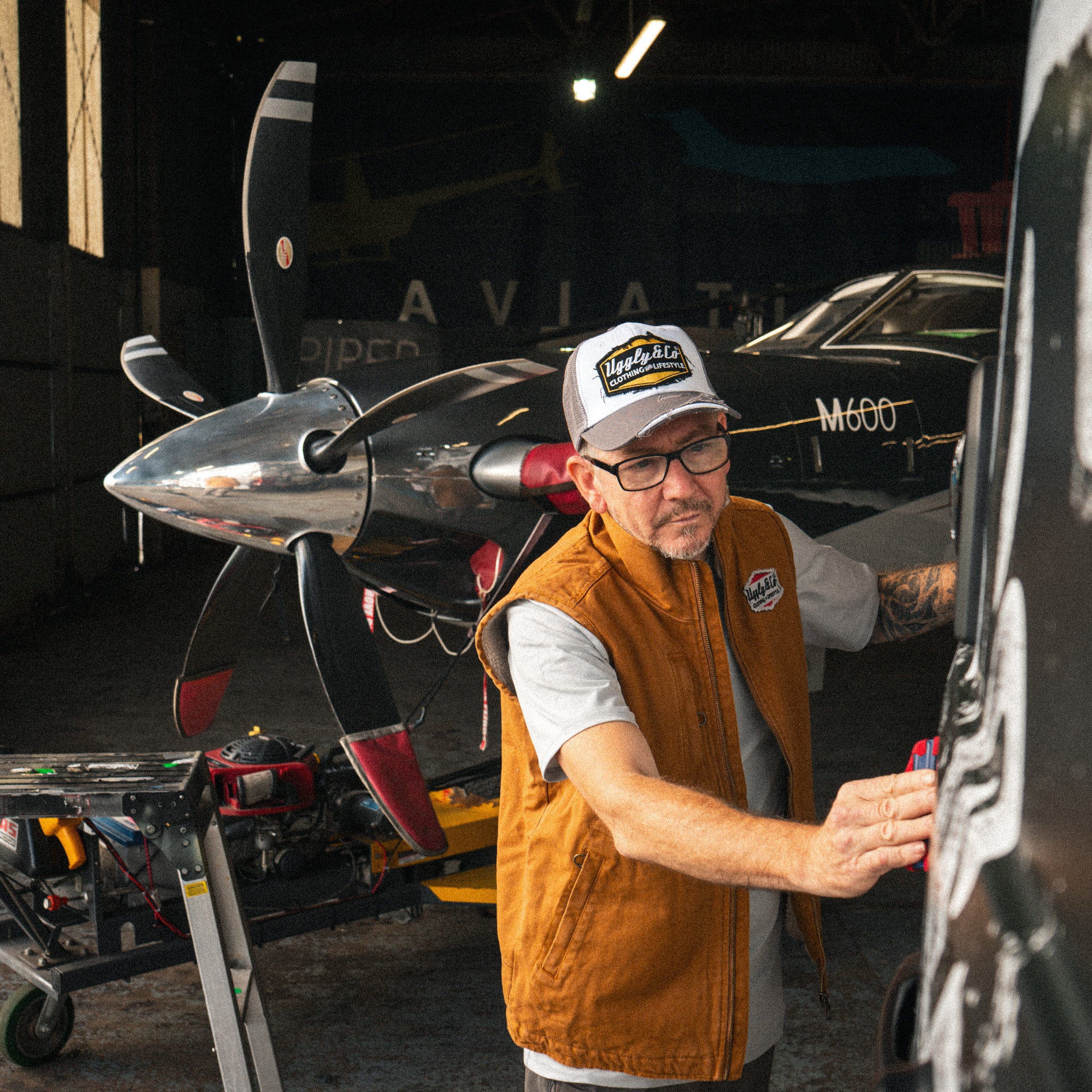 Mens Grey & White Diamond Trucker Cap worn inside an aircraft hangar during a vehicle wrap.