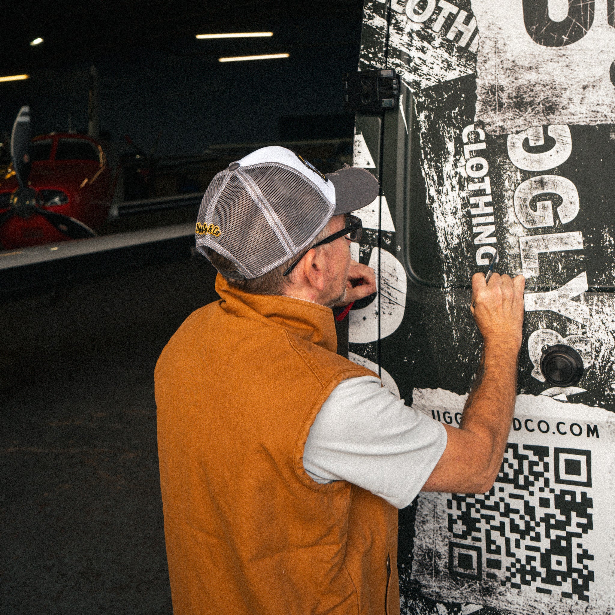 Grey and white vintage trucker cap worn by a man installing vinyl graphics on a van.