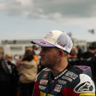 Side view of Mitch Reese wearing a white and purple trucker hat with Uggly&Co diamond logo on the front, a mesh back and Mitch Rees Racing logo on the side
