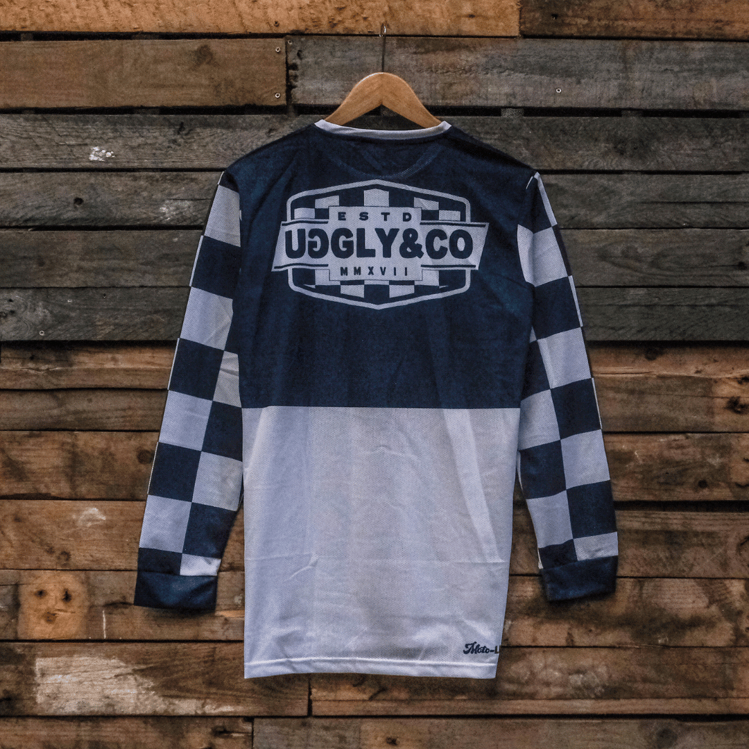 Backwards facing checkered long-sleeve MX shirt with an Uggly&Co brand logo on a wooden background