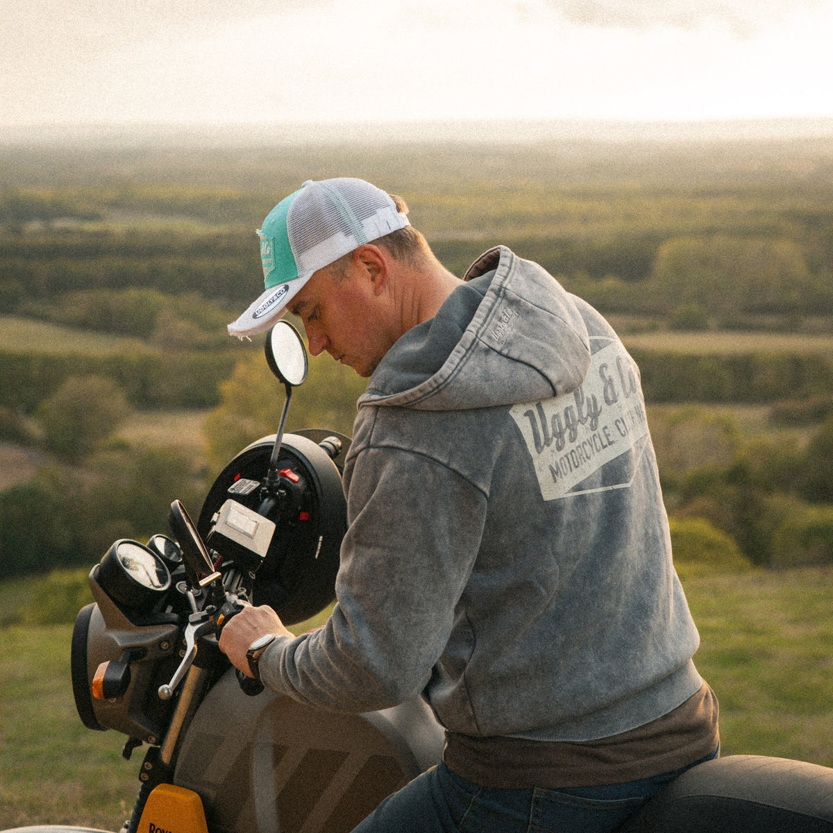 Motorcyclist in a turquoise and white trucker hat with a Royal Enfield Scram 411 scrambler