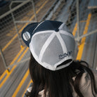 Uggly&Co Night Blue and Gold Diamond Trucker Hat worn by a female model in a racing grandstand