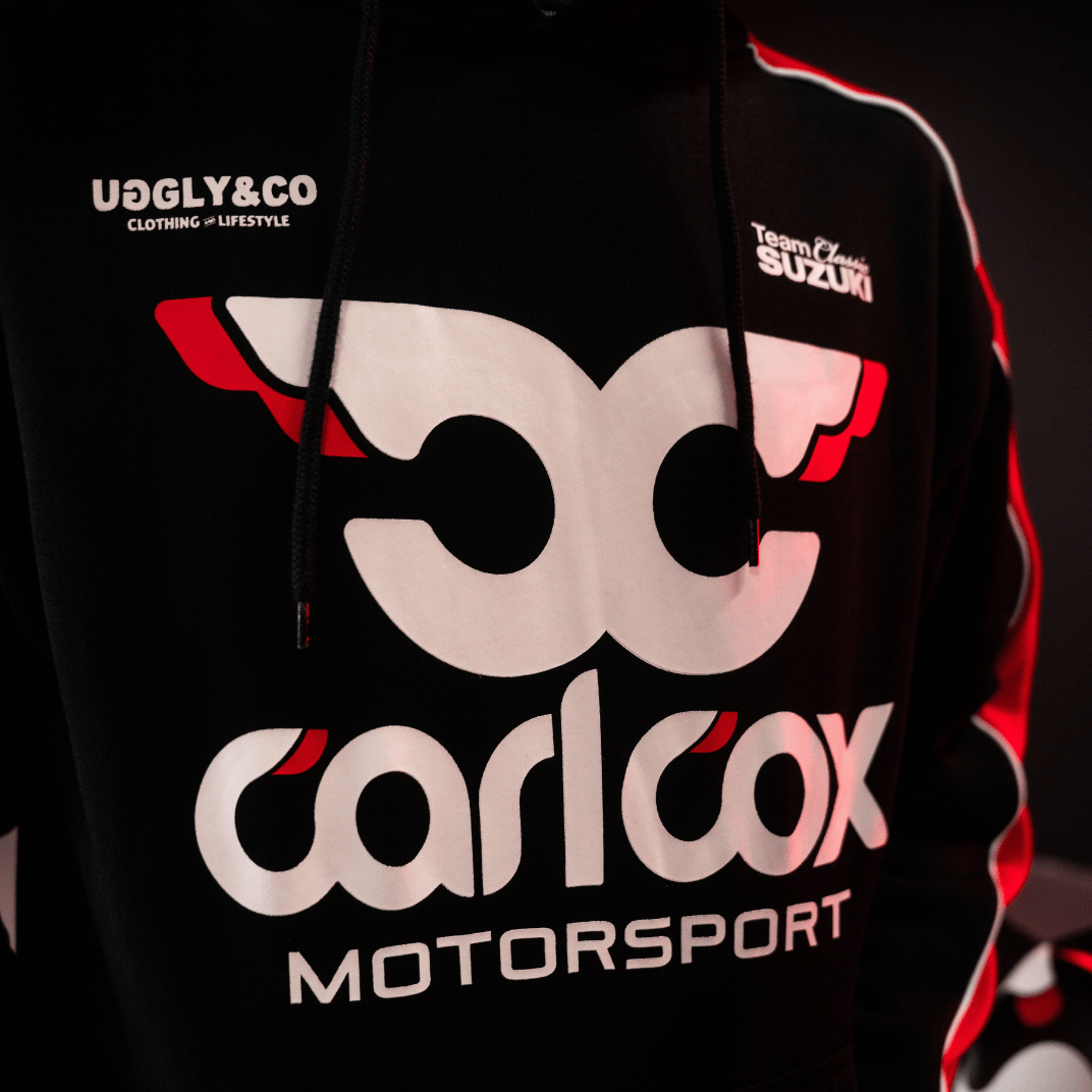 Close up of the front detailing on a black hoodie with red sleeves featuring Carl Cox Motorsport, Team Classic Suzuki and Uggly&Co branding