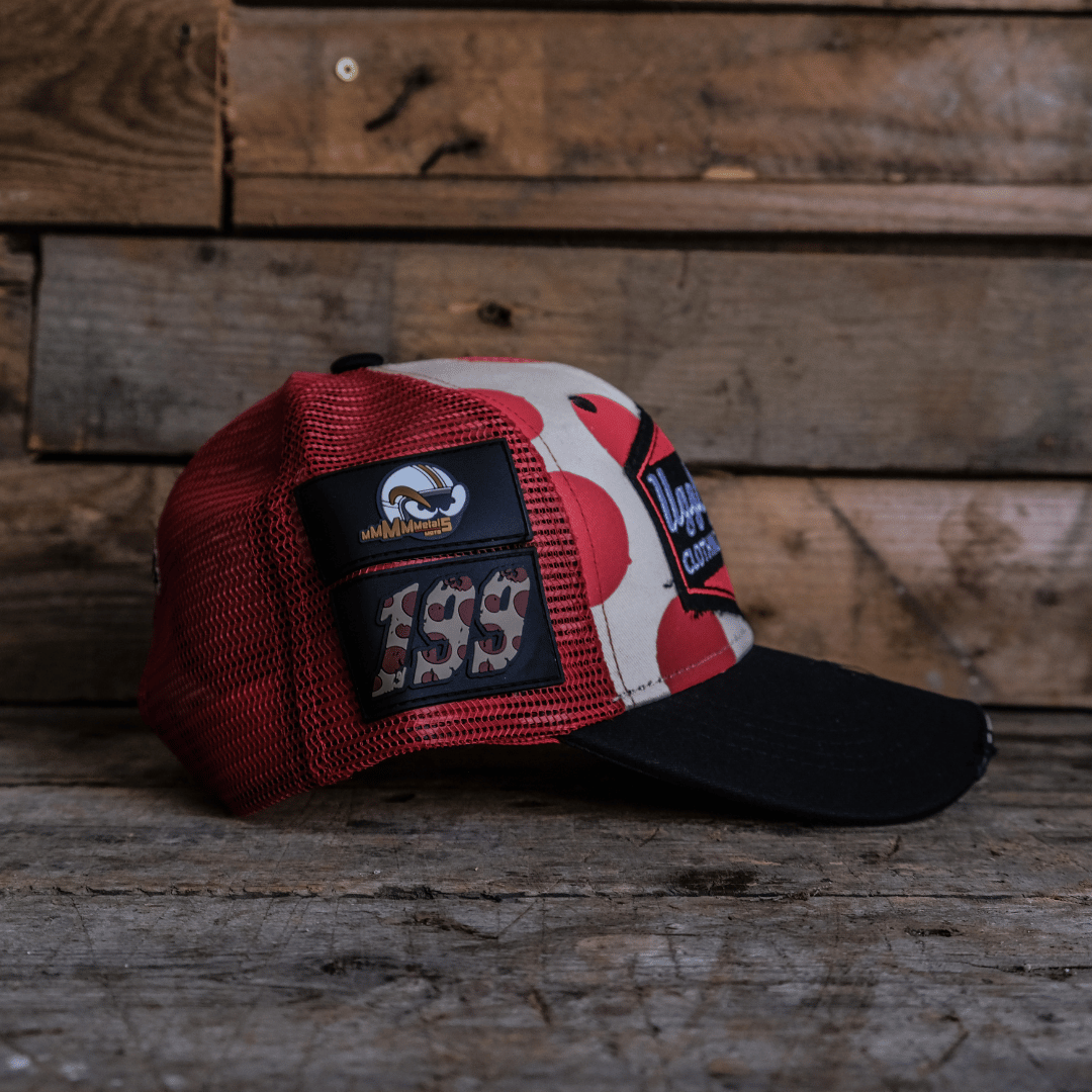Side view facing right of a trucker hat with red and white polka dot design and signature Uggly&Co logo on a wooden background