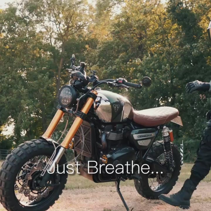 Male motorcyclist wearing an acid wash hoodie on a Triumph Scrambler in warm evening light.