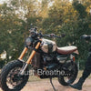 Male motorcyclist wearing an acid wash hoodie on a Triumph Scrambler in warm evening light.