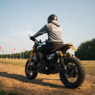 Man wearing an acid wash hoodie sitting on a Triumph Scrambler motorcycle at sunset.