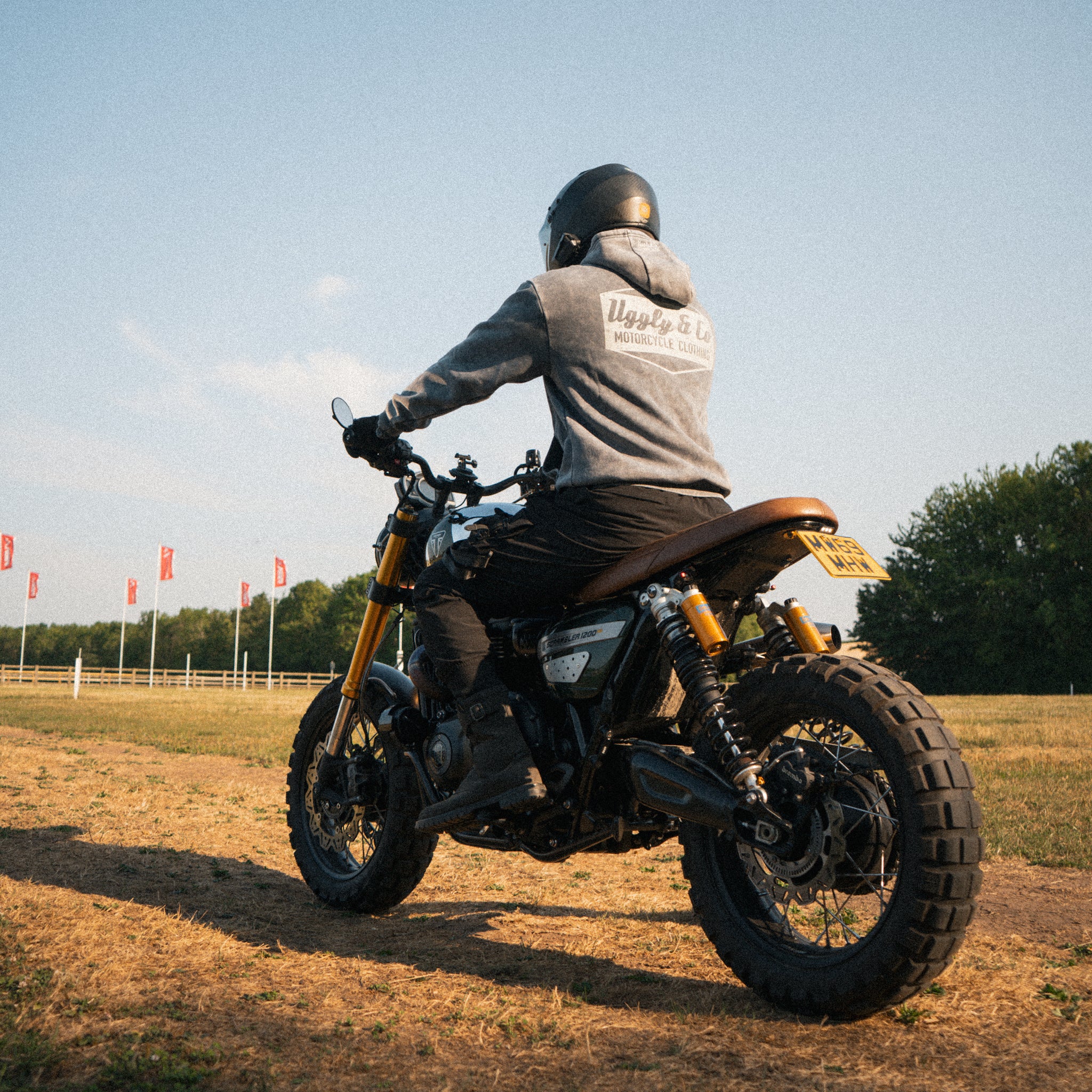 Man wearing an acid wash hoodie sitting on a Triumph Scrambler motorcycle at sunset.