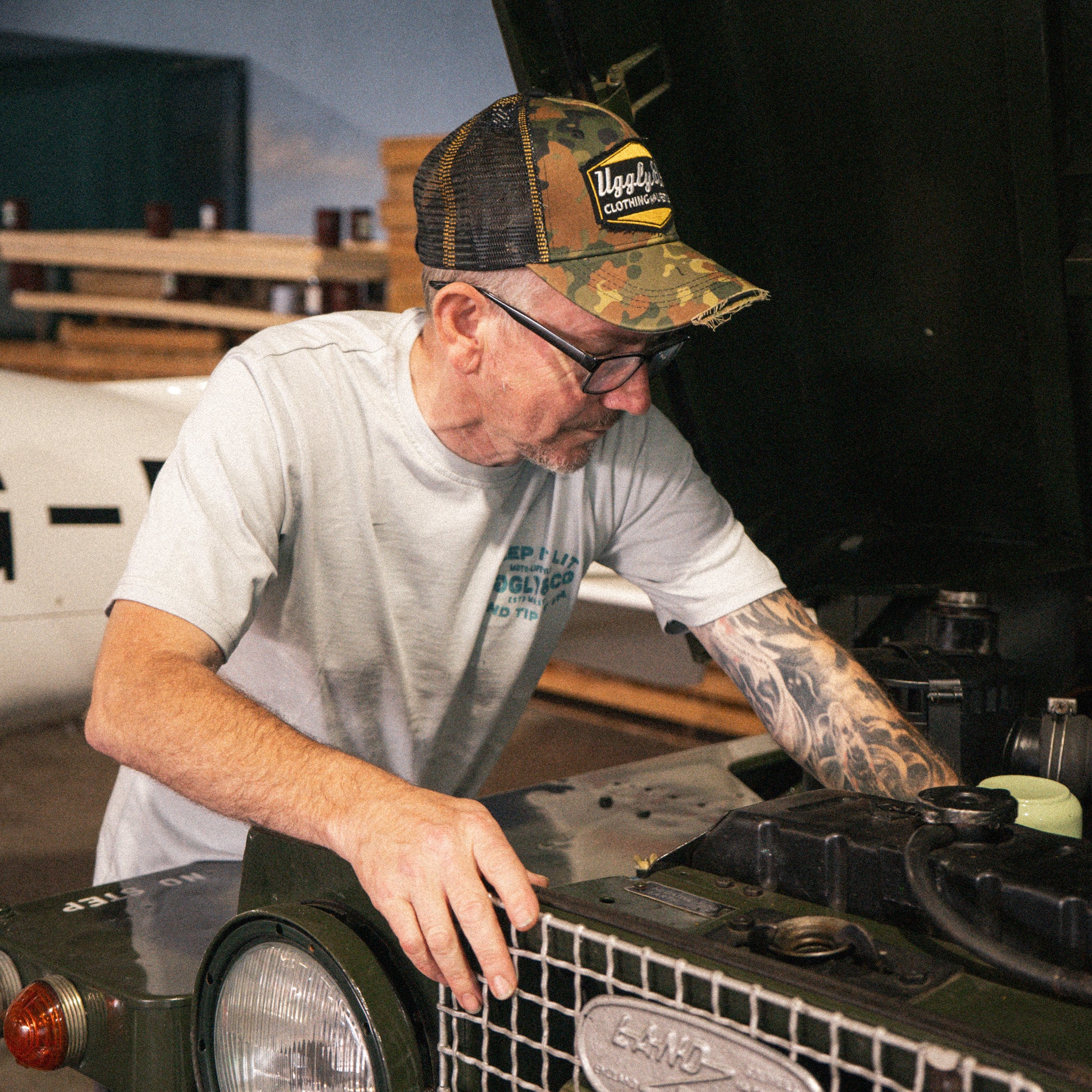 Uggly & Co Green Camo Diamond Trucker Hat worn by a man working on a Land Rover.