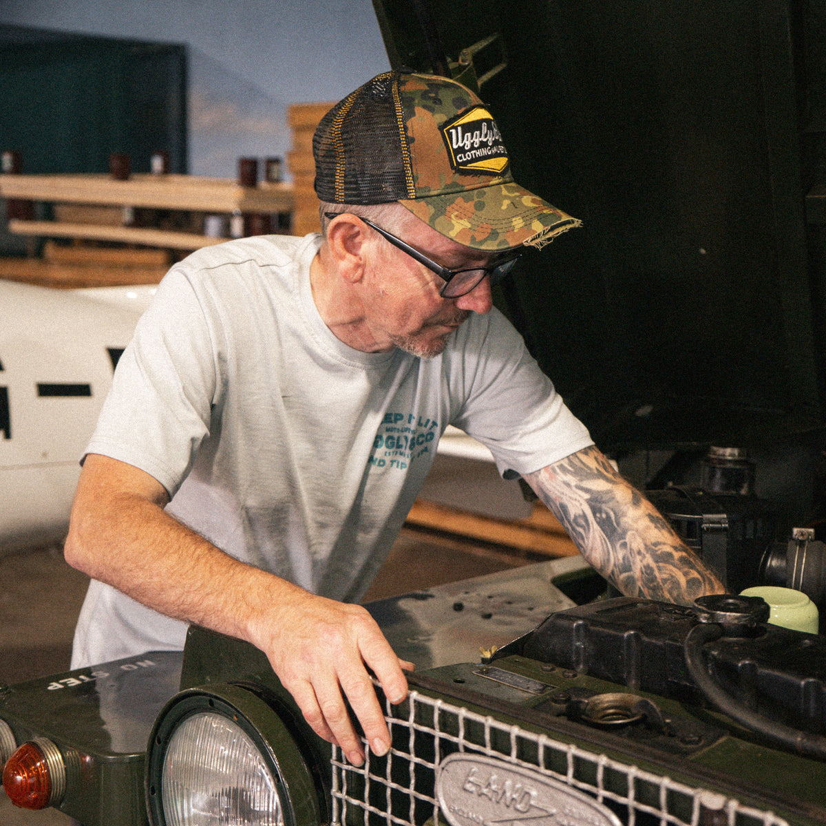 Uggly & Co Green Camo Diamond Trucker Hat worn by a man working on a Land Rover.