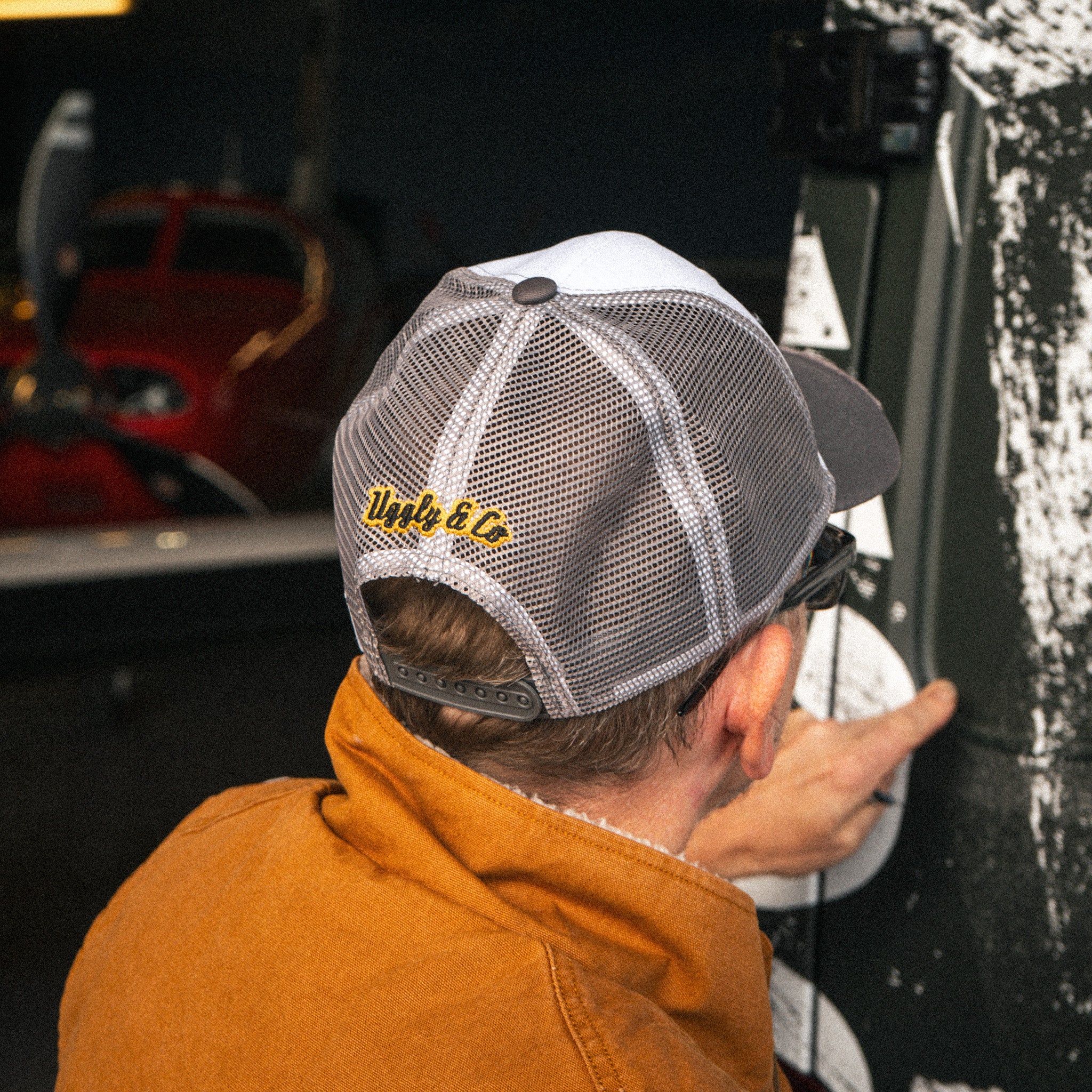 Uggly & Co Grey & White Diamond Trucker Cap photographed in an industrial aircraft hangar.