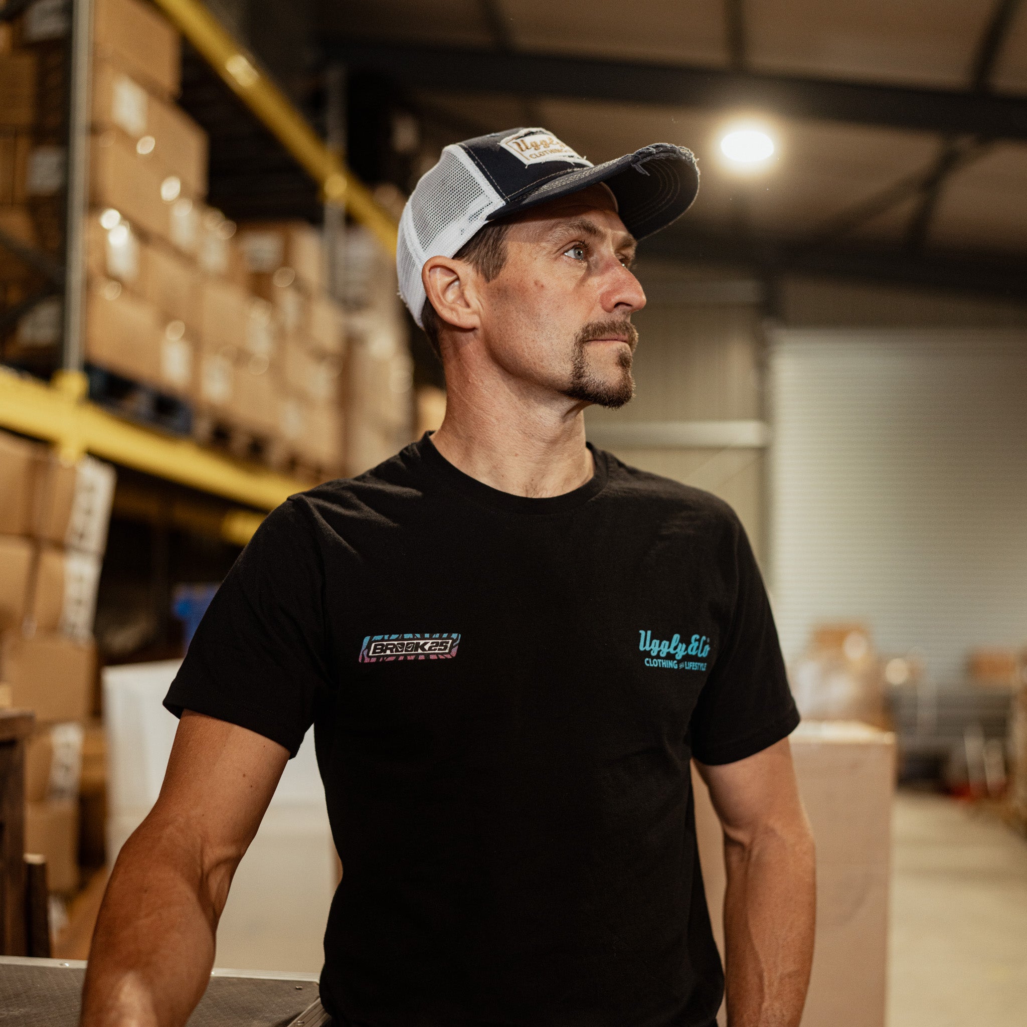 Front view of a model wearing a Josh Brookes signature diamond black t-shirt with blue and red Uggly&Co diamond logo with a blurred background