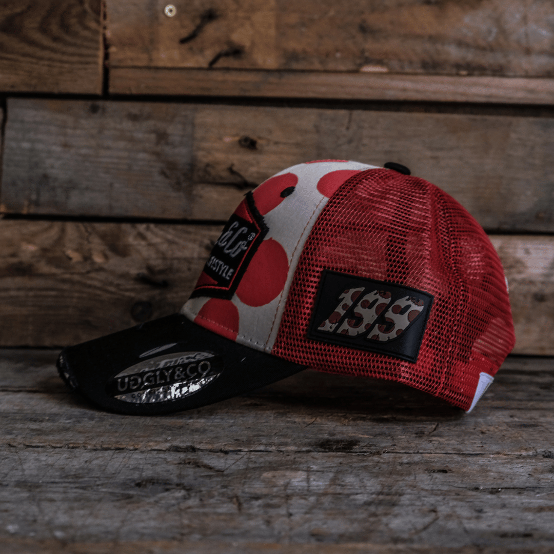 Side view of a trucker hat with red and white polka dot design and signature Uggly&Co logo on a wooden background