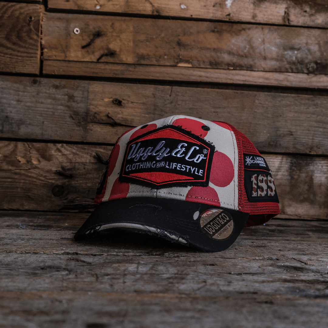Front view of a trucker hat with red and white polka dot design and signature Uggly&Co logo on a wooden background