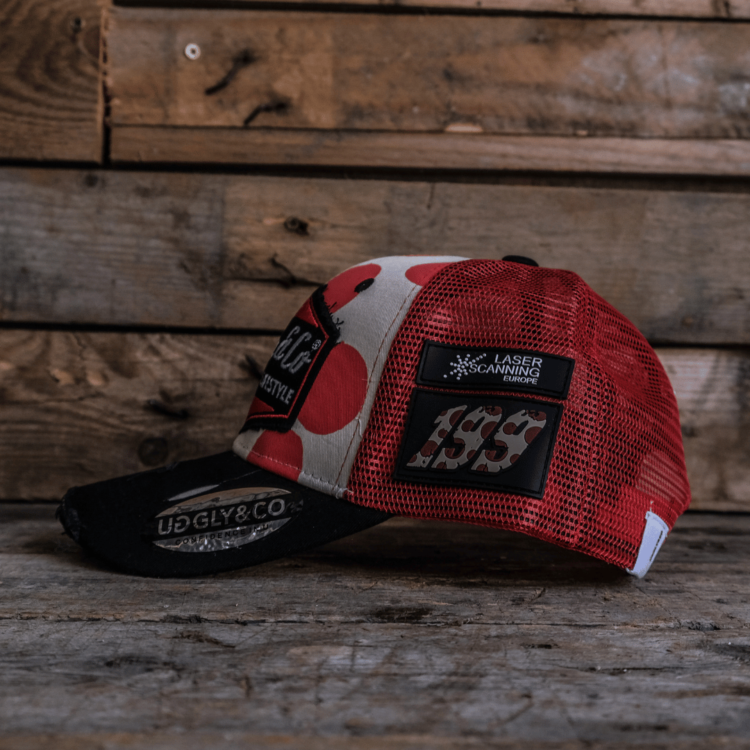 Side view of a trucker hat with red and white polka dot design and signature Uggly&Co logo on a wooden background with 199 logo on the side